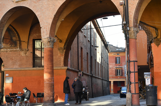 Arched walkway in a historic Italian street with people and outdoor seating.