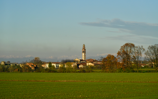 Charming Italian village with a prominent tower surrounded by green fields and hills.