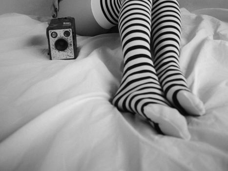 Artistic shot of striped leggings and vintage camera on a bed.