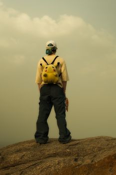 A young adult stands on a mountaintop with a Pikachu backpack, looking at the horizon.