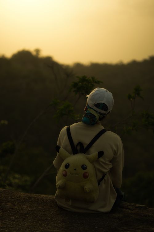 Free Person with Pikachu backpack enjoys a peaceful sunset view in nature. Stock Photo