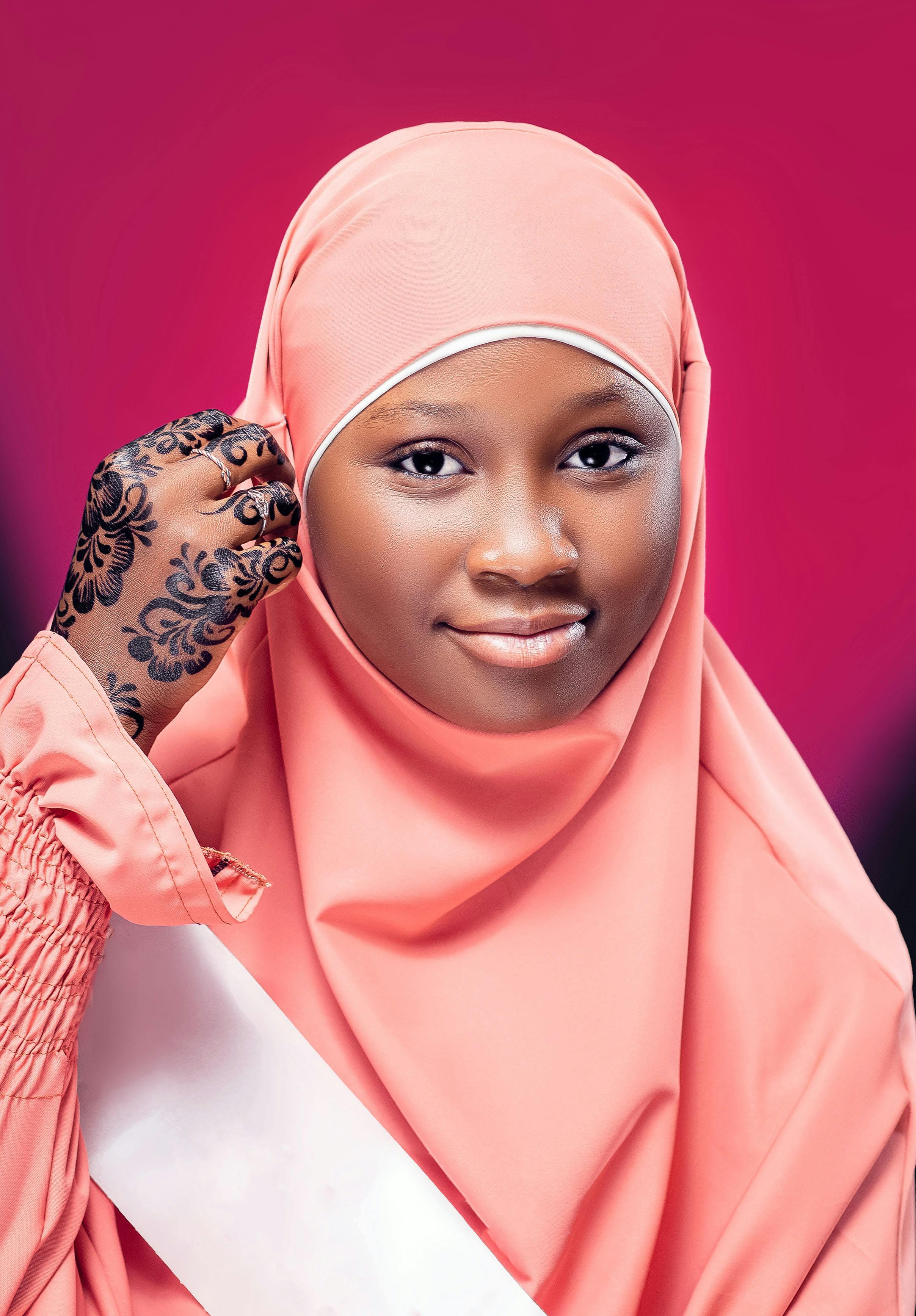 Captivating portrait of a young woman in a pink hijab featuring intricate henna art on her hand.
