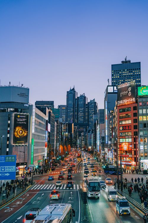 Free Bustling street scene of Shinjuku, Tokyo at dusk with illuminated skyscrapers and traffic. Stock Photo