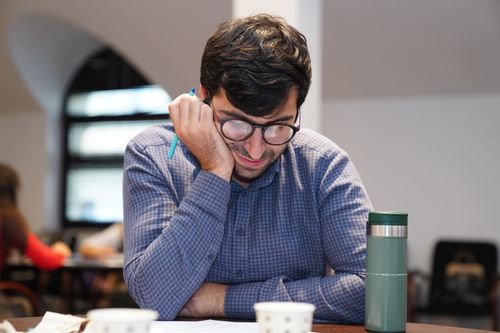 Free Adult male deep in concentration while reading at a desk indoors, with a coffee cup and tumbler nearby. Stock Photo