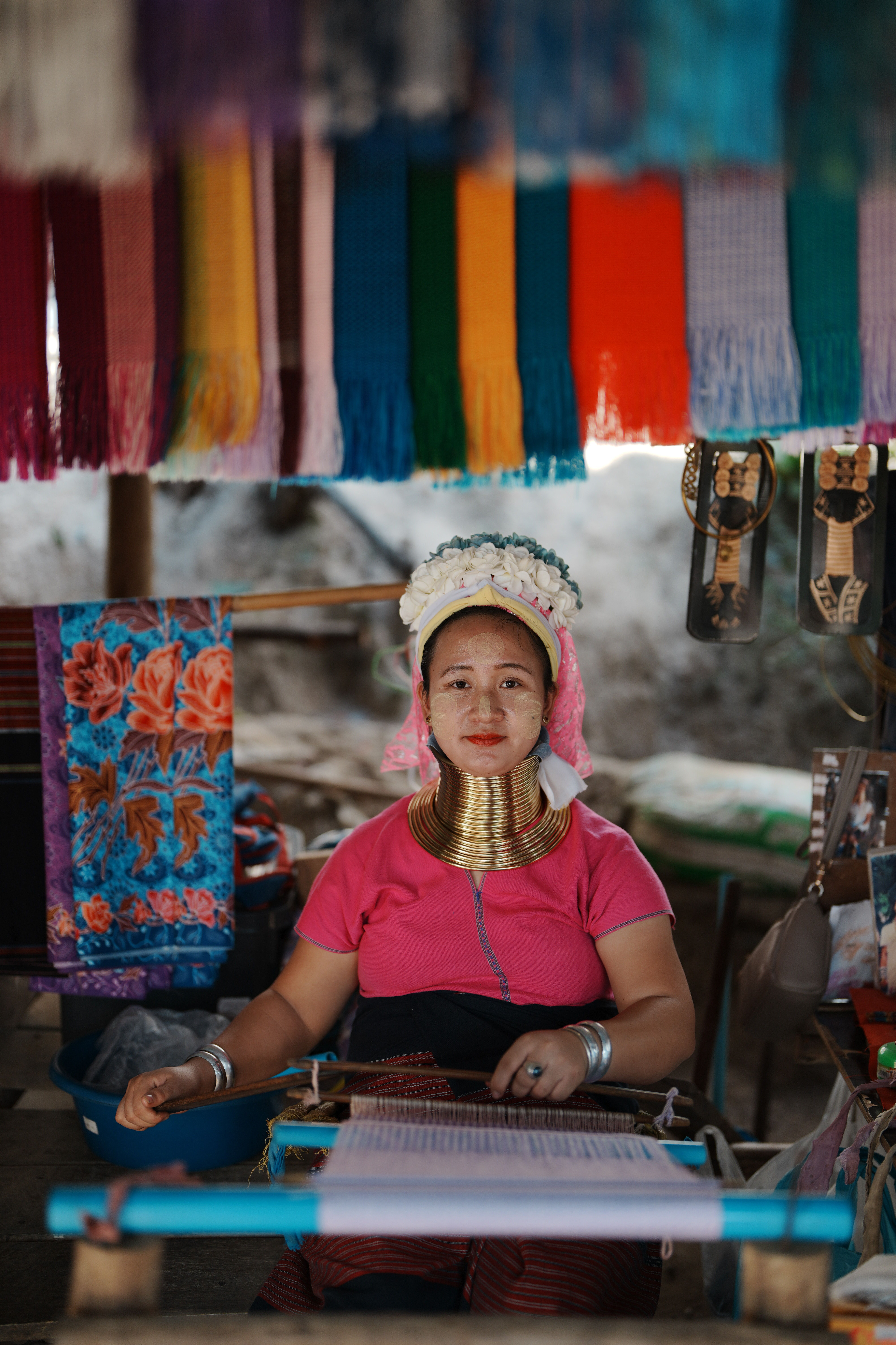 A long neck woman in traditional attire weaving at a colorful market stall, showcasing ethnic culture.