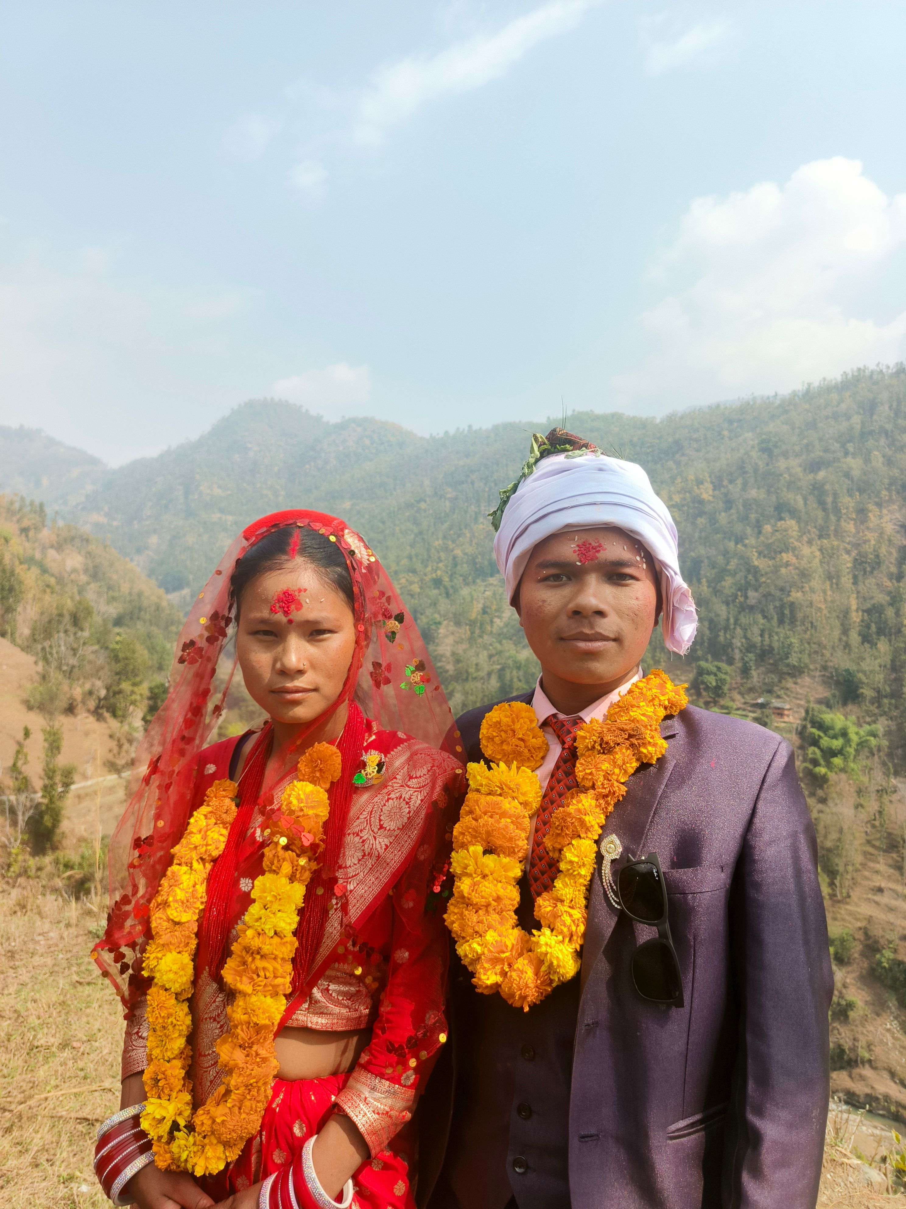 Bride and groom in colorful traditional attire during a Nepali wedding ceremony outdoors.
