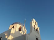 一张圣托里尼岛传统白色教堂的低角度视图，教堂带有蓝色圆顶，天空晴朗