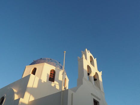 一张圣托里尼岛传统白色教堂的低角度视图，教堂带有蓝色圆顶，天空晴朗