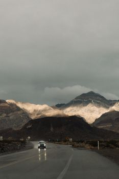 A car drives along a wet road in Death Valley with dramatic mountain scenery.