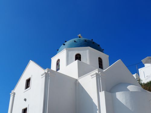Free A stunning low angle shot of a white church with a blue dome on a sunny day in Santorini. Stock Photo