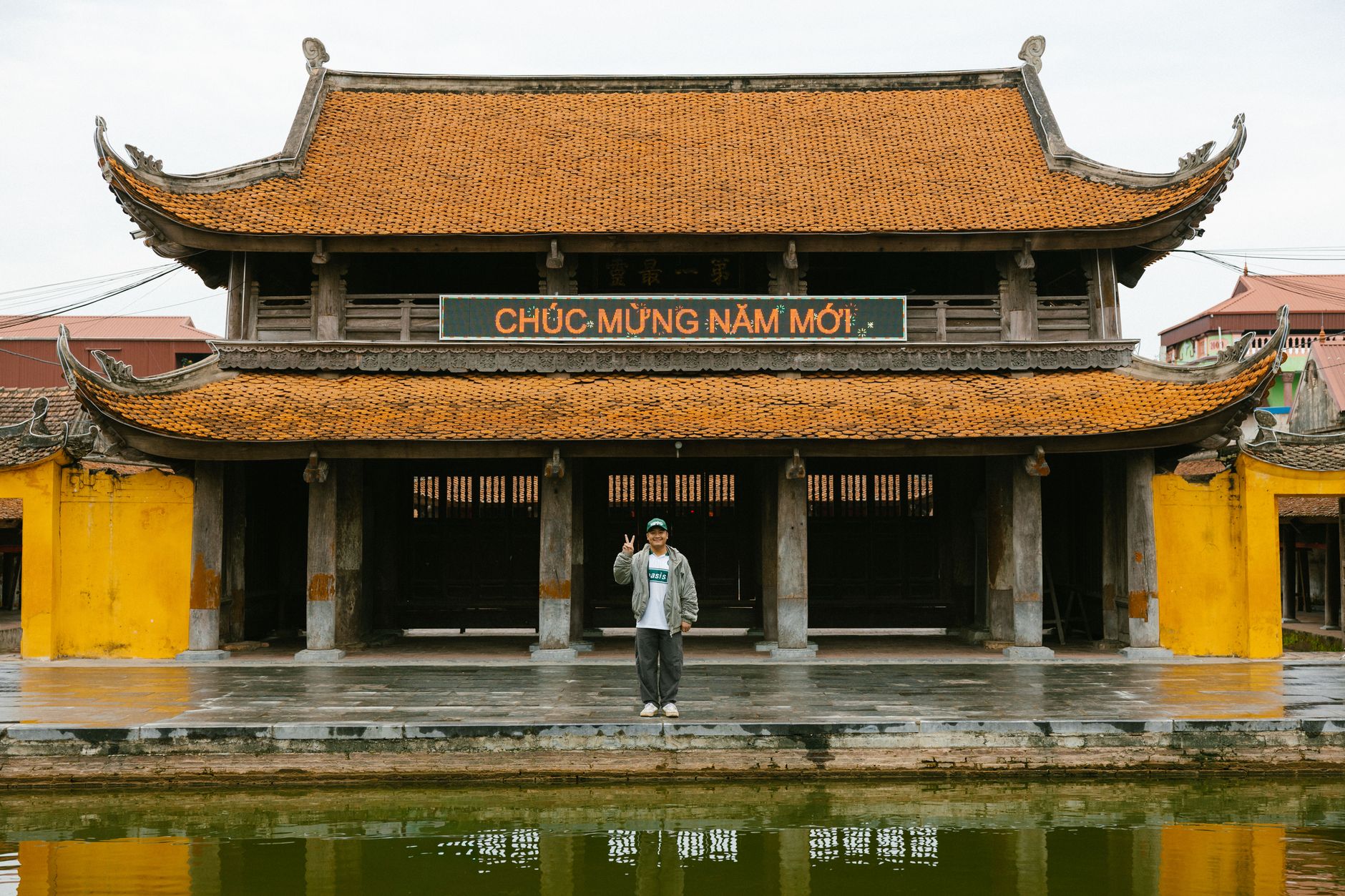 A person standing in front of a traditional Vietnamese temple with intricate roof design and festive sign.