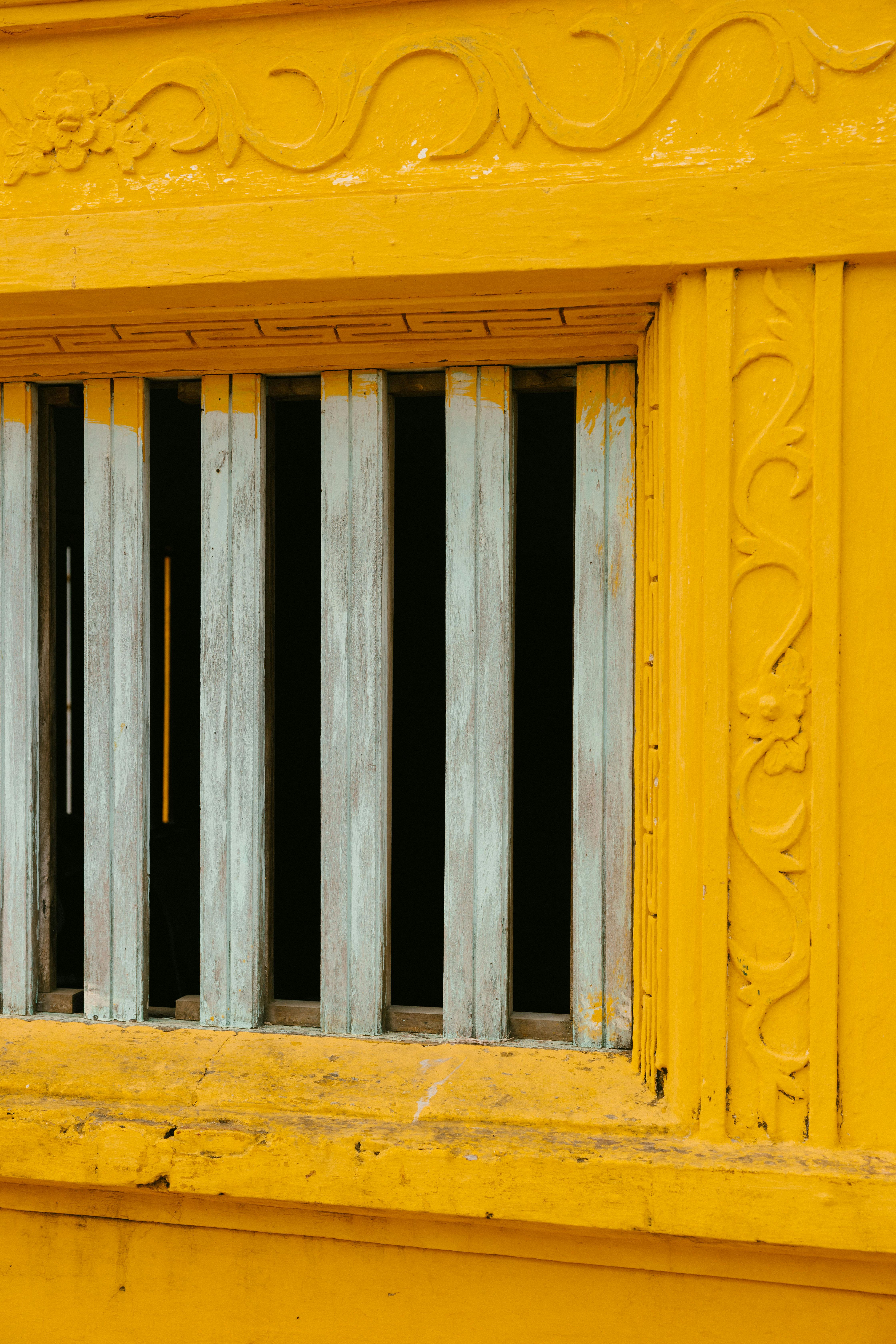 Gratis Primo piano di una finestra gialla decorata con intagli decorativi e barre di legno invecchiato. Foto a disposizione
