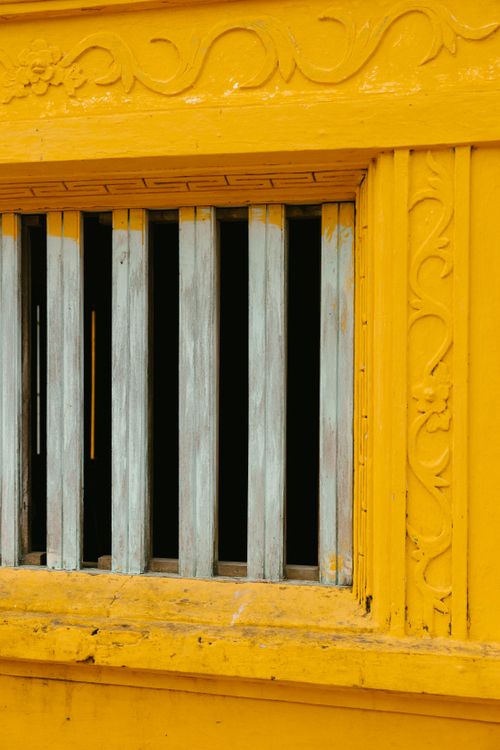 Free Close-up of an ornate yellow window with decorative carvings and aged wooden bars. Stock Photo