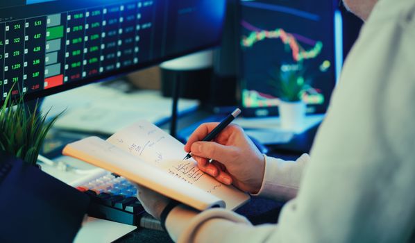 Person analyzing financial data on screens, making notes. Ideal for business and finance themes.