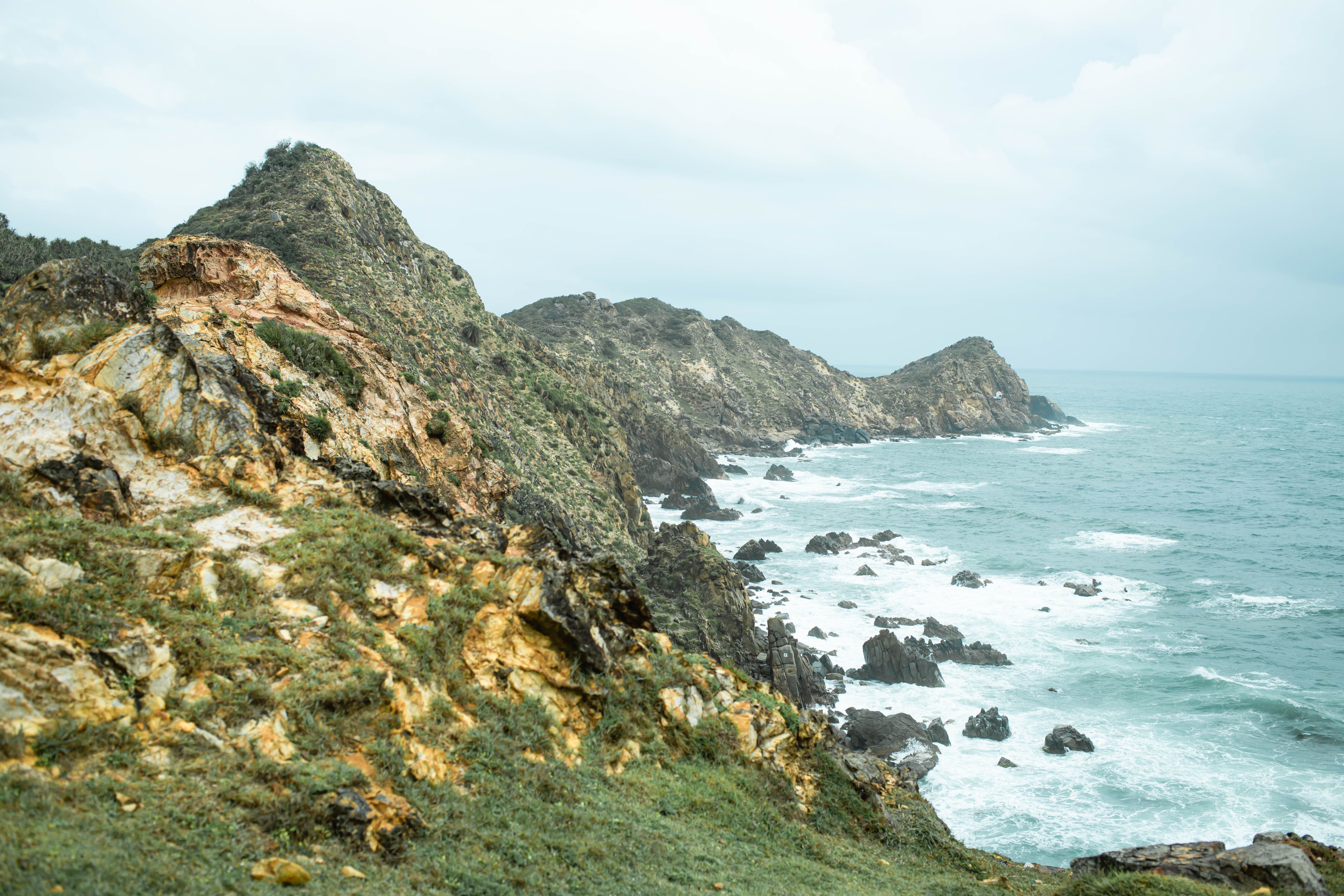 A dramatic seascape featuring rugged cliffs along a rocky coastline under a cloudy sky.