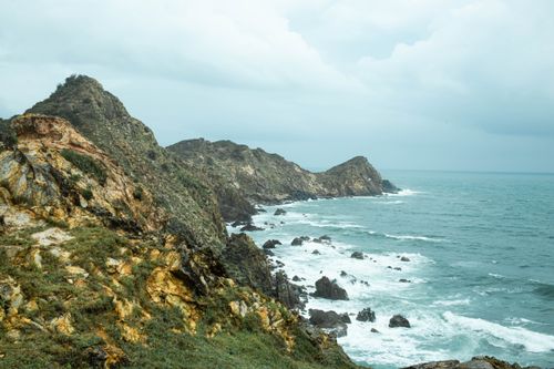 Free Breathtaking view of rugged cliffs and crashing waves under a cloudy sky. Stock Photo