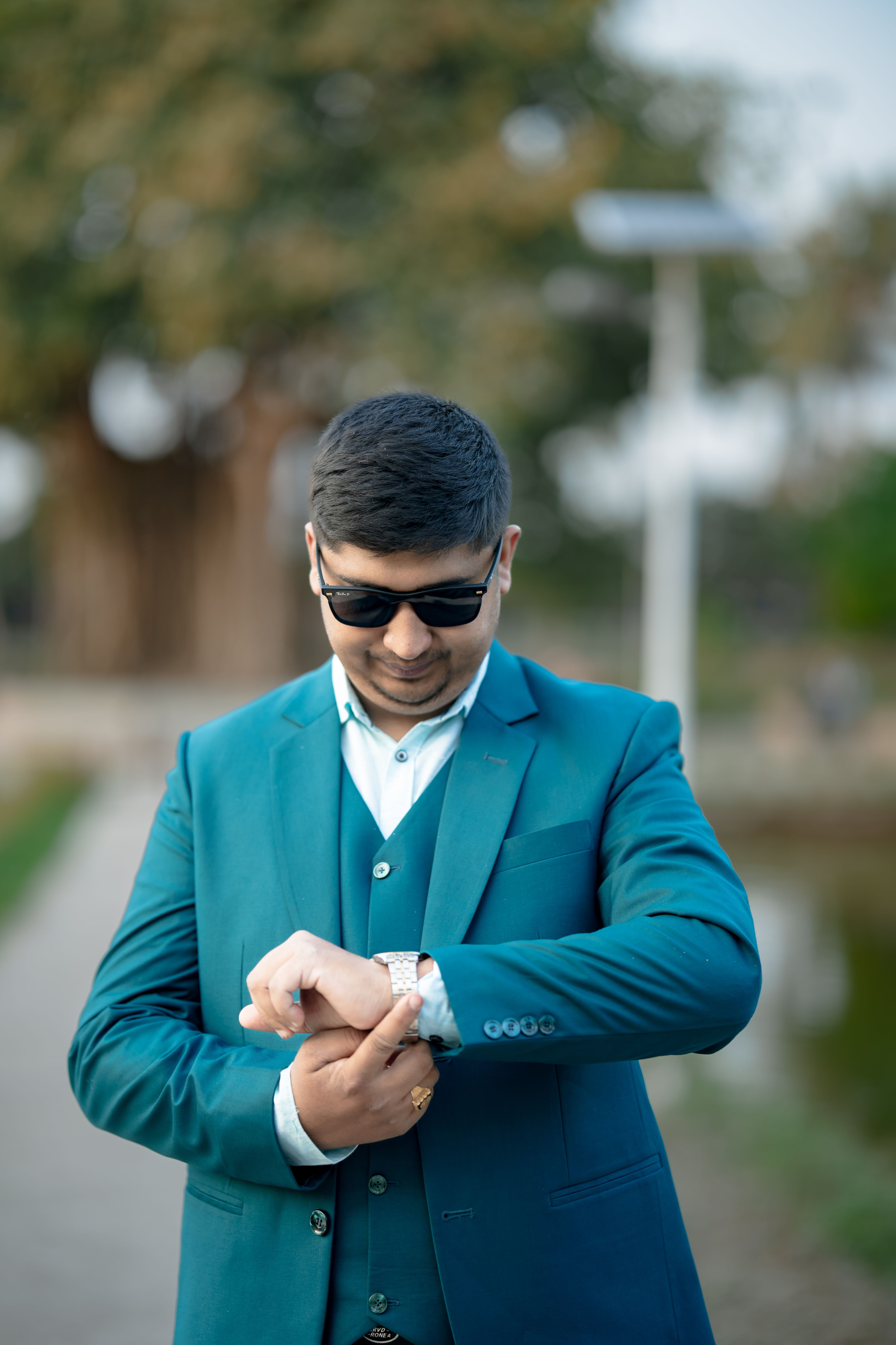 Gratis Un giovane uomo in abito verde acqua e occhiali da sole controlla l'orologio all'aperto in una giornata di sole. Foto a disposizione
