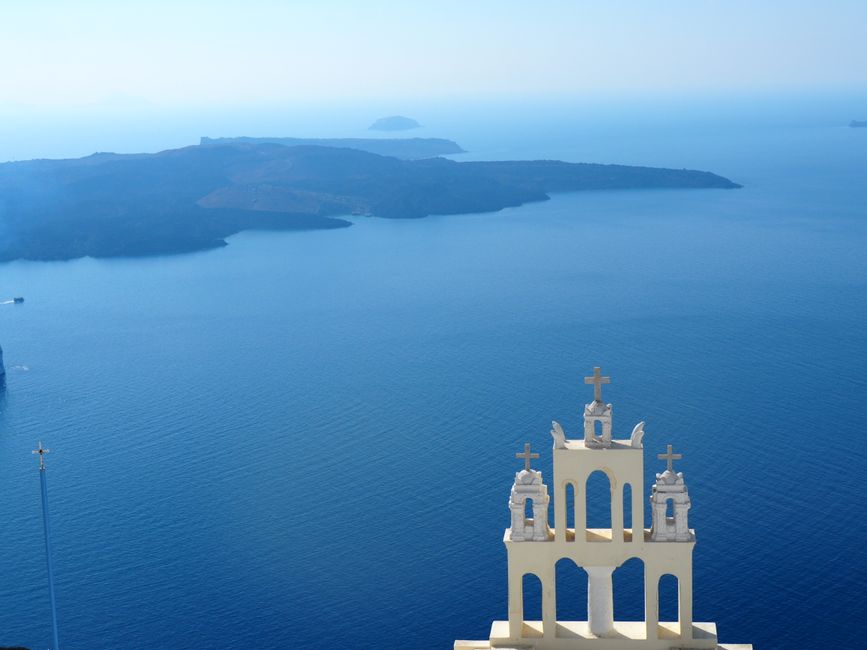 Santorini church tower overlooking the Aegean Sea with distant islands in view.