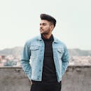 一名身穿牛仔夹克的时髦年轻男性模特，以都市风景为背景，展现现代时尚