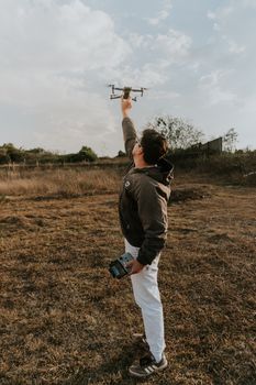 A man prepares to launch a drone in an open grassy field under a cloudy sky.