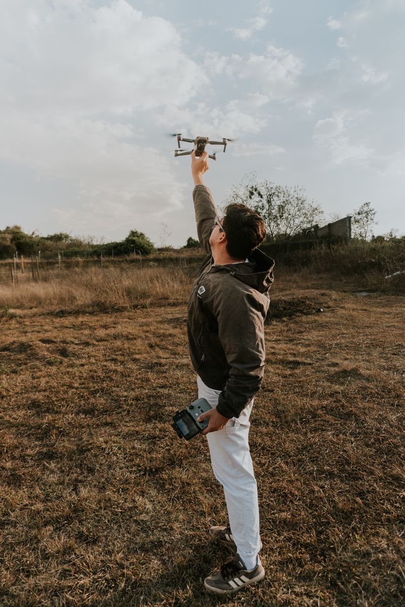 A man prepares to launch a drone in an open grassy field under a cloudy sky.