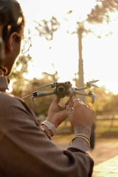 Adult man preparing a drone for flight in a sunny outdoor park setting.