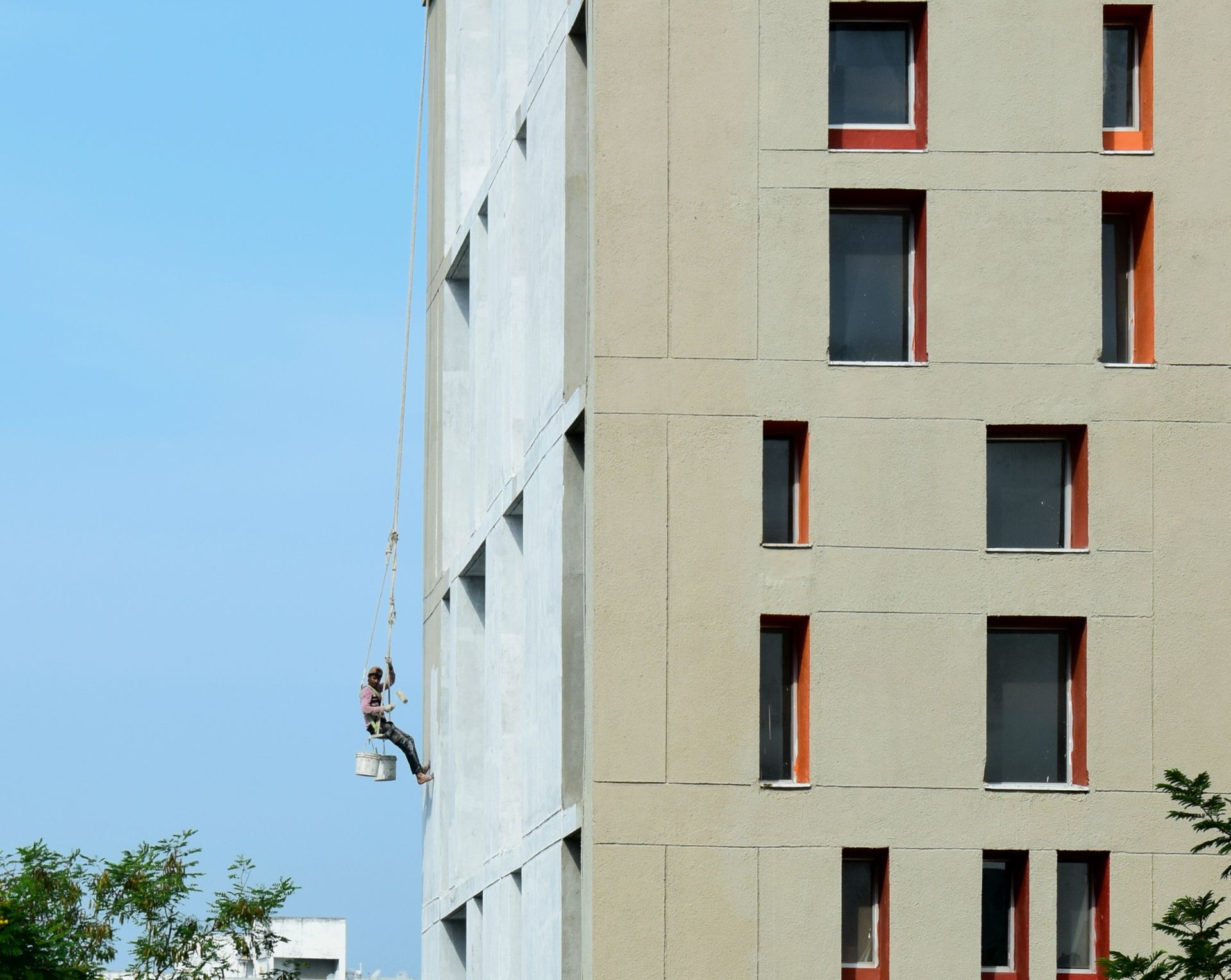 Operario suspendido en silleta pintando la fachada de un edificio en torre