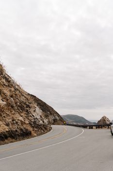 A winding road along a rocky coastline with a car and cloudy sky, capturing the essence of a road trip adventure.