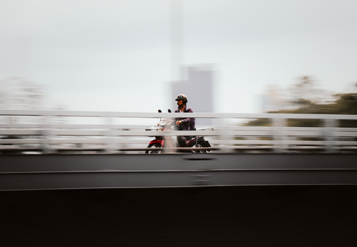 A motorcyclist rides across a bridge in Bangkok with a dynamic motion blur effect.