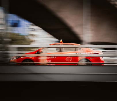 Motion blur of a red taxi speeding through the bustling streets of Bangkok, Thailand.
