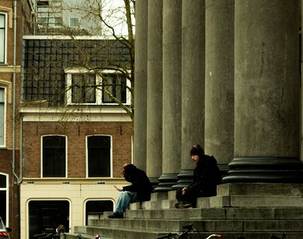Two individuals sitting on historic building steps, urban setting.