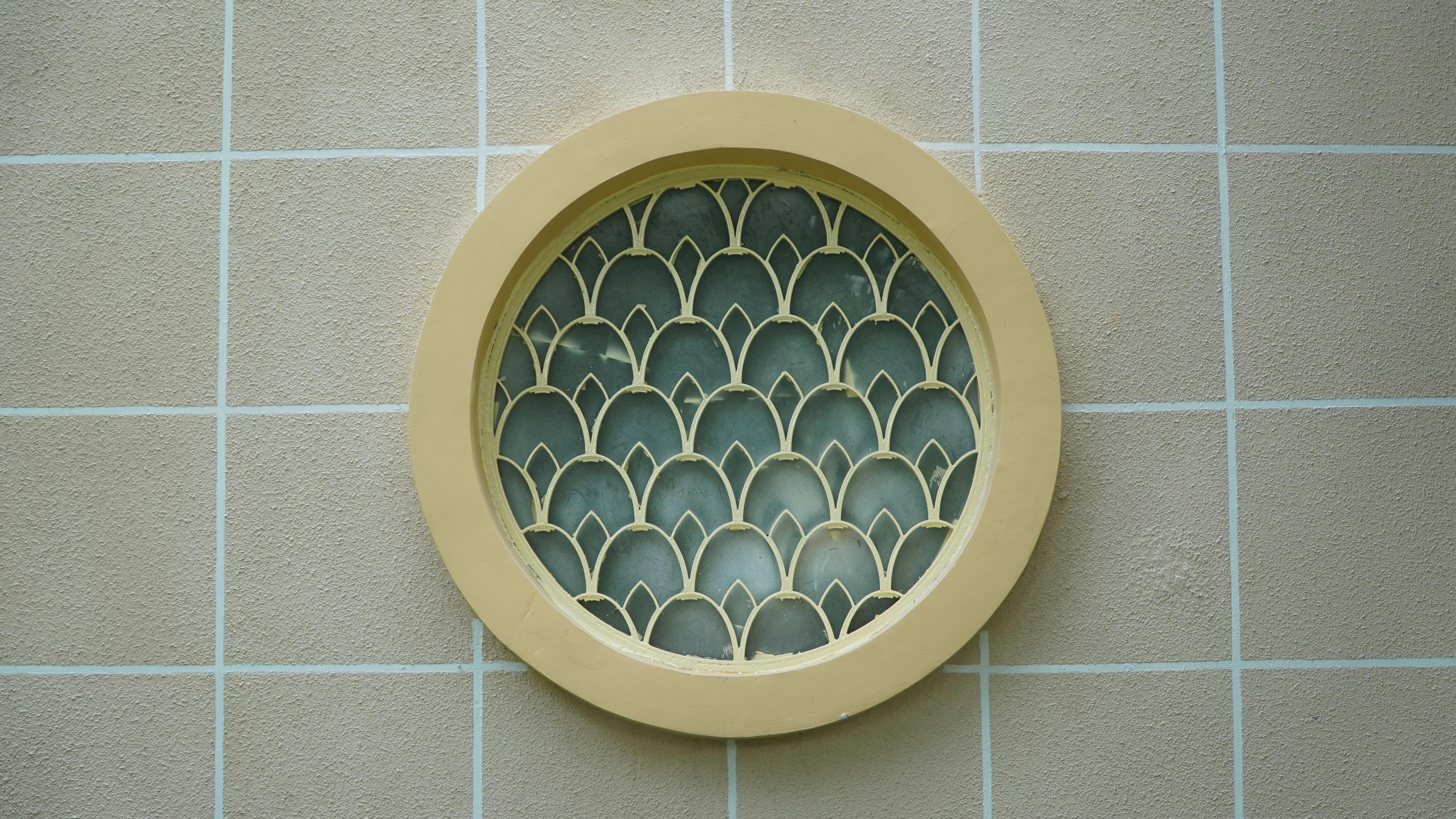 Free A round decorative window with a geometric grill on a tiled wall, featuring a modern artistic design. Stock Photo