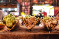 Close-up of three chicken tacos with guacamole, herbs, and onions in a restaurant setting.