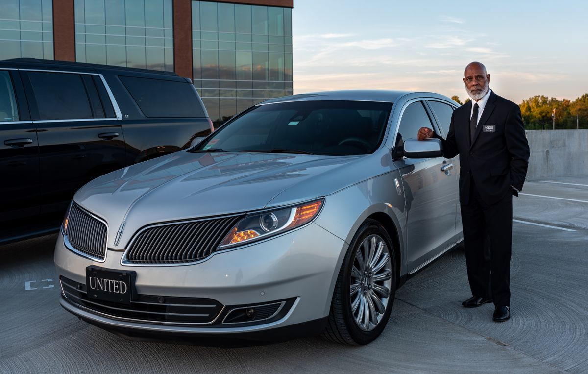 Professional chauffeur beside a luxury car