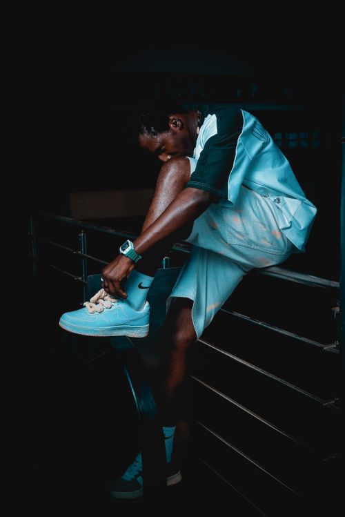 Free Young man in athletic wear laces sneakers in a moody urban setting. Stock Photo