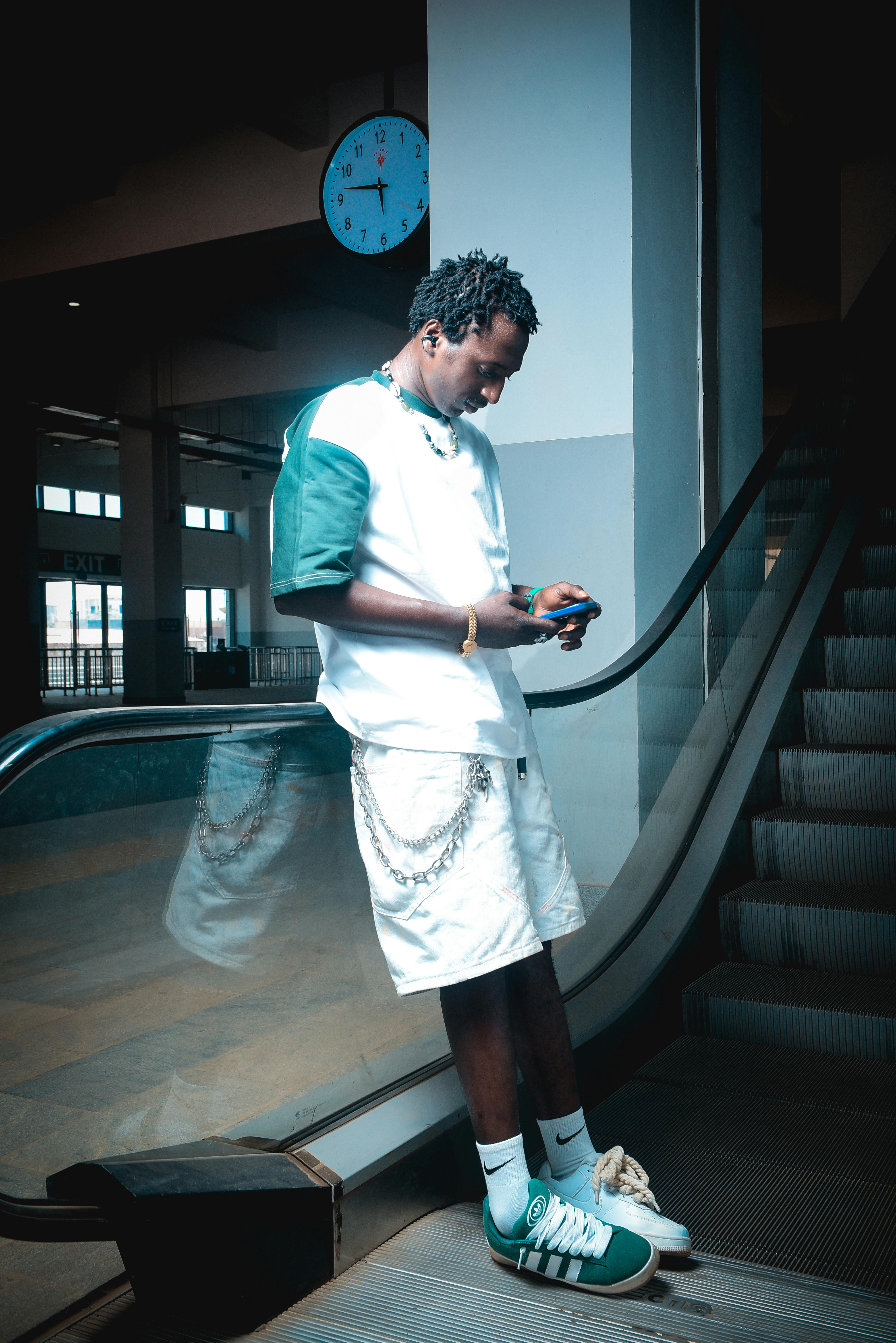 Gratis Giovane adulto alla moda che usa lo smartphone accanto a una scala mobile in un edificio. Foto a disposizione