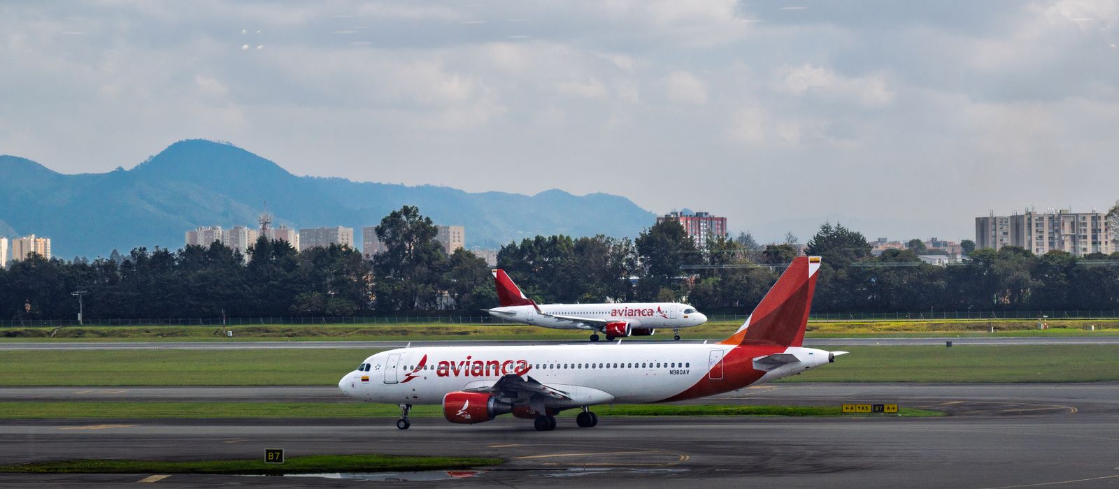 Avianca passenger aircraft on the runway at Bogotá, Colombia airport with city and mountains in background. — flights from Cancun to Bogota