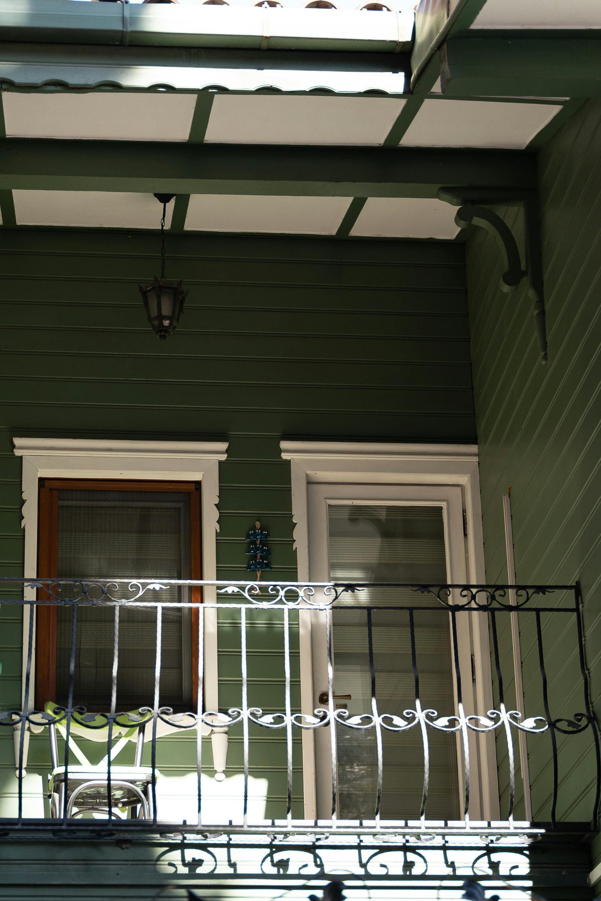 Gratis Sjarmerende trebalkong med jernrekkverk og grønne paneler i direkte sollys. Arkivbilde