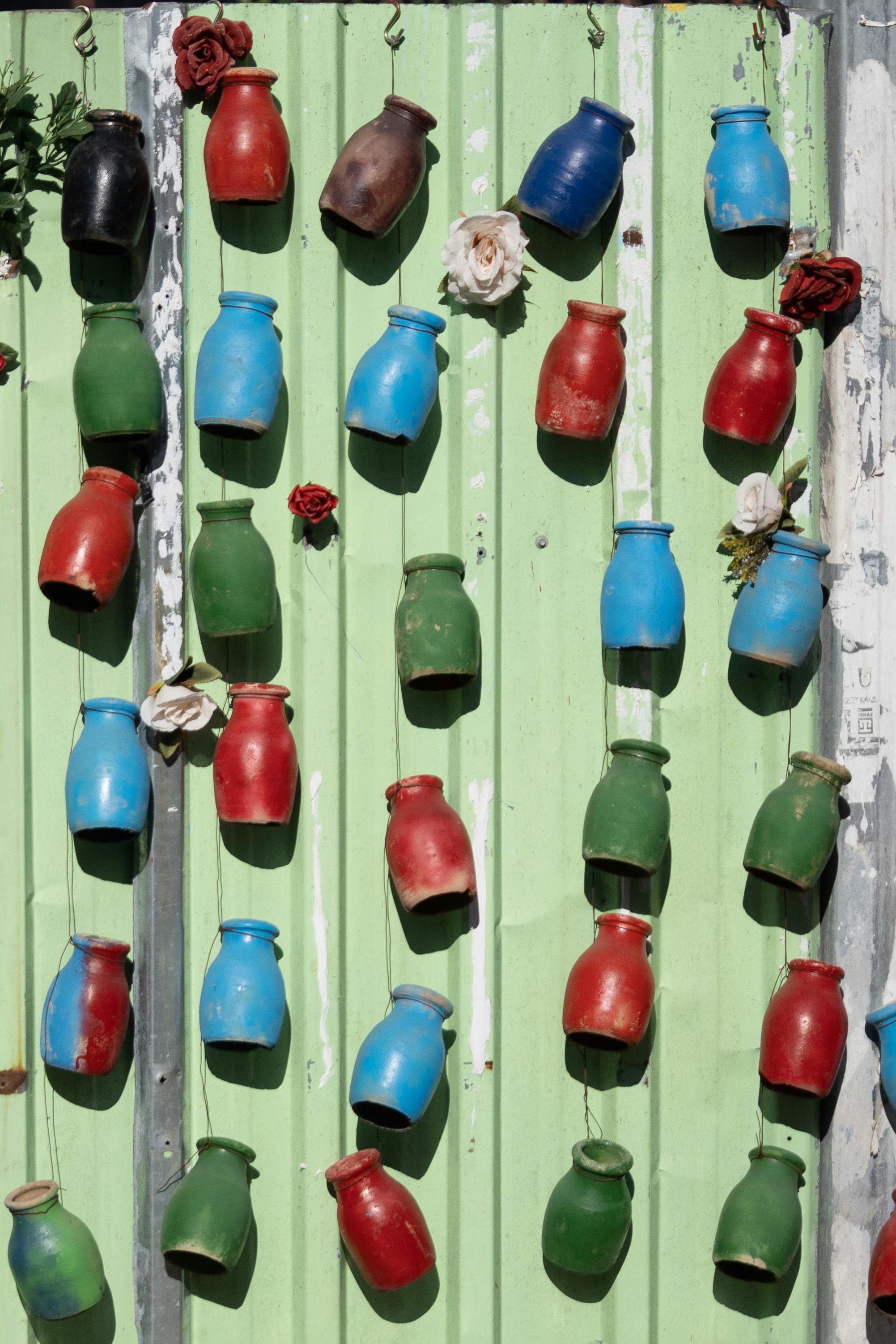 Gratis Vasi dai colori vivaci, blu, rossi e verdi, decorano una parete verde rustica, creando un'esposizione artistica all'aperto. Foto a disposizione