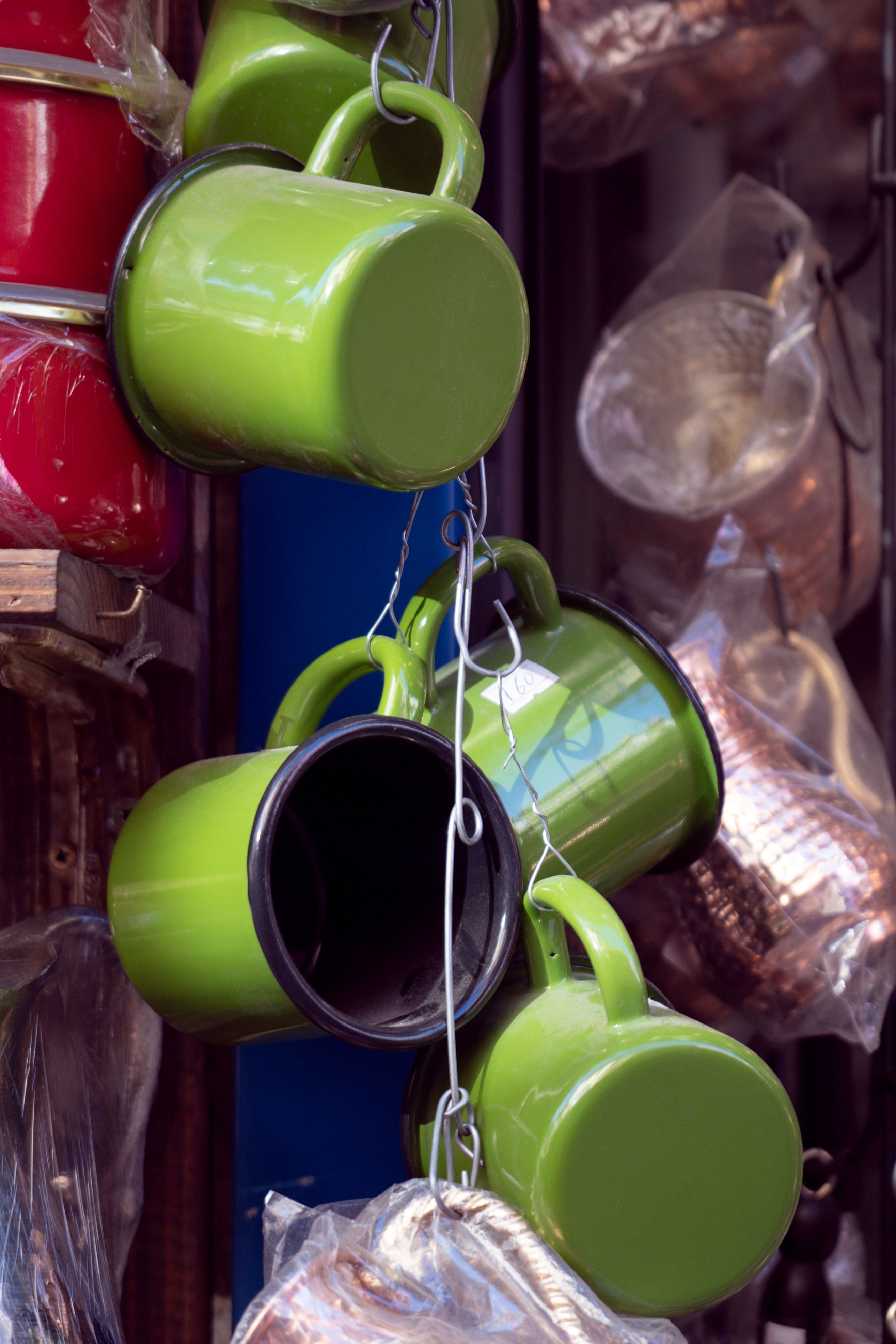 Close-up of colorful metal mugs displayed in a market, with focus on vibrant green hues.
