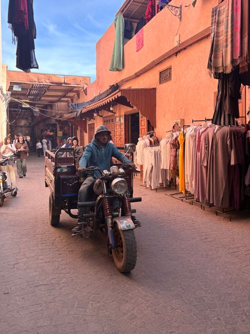 Free Vibrant street scene in Marrakesh souk with motorcyclist amid colorful stalls. Stock Photo