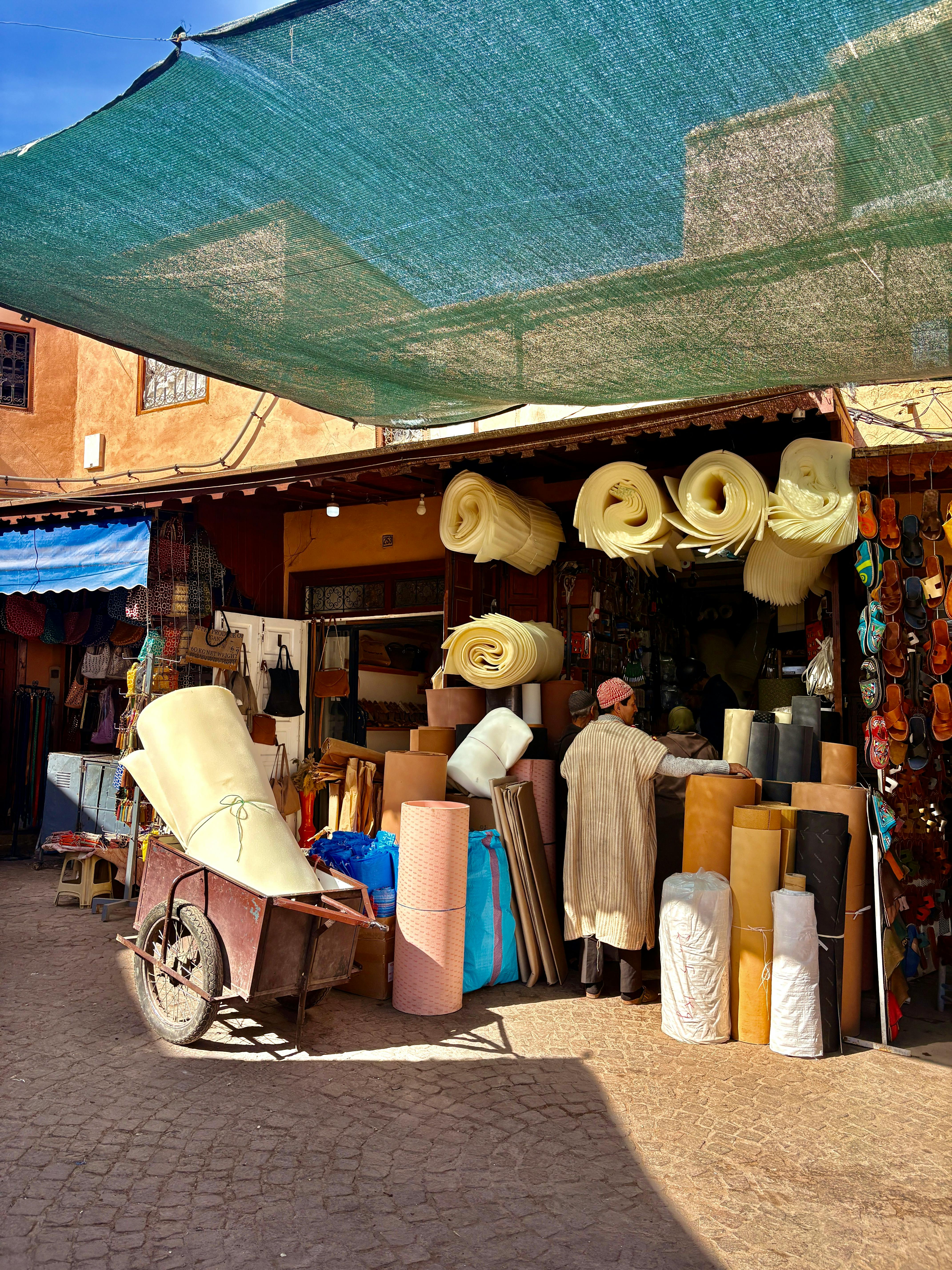 Boutique colorée du souk de Marrakech, proposant divers articles et textiles sous une verrière ensoleillée.