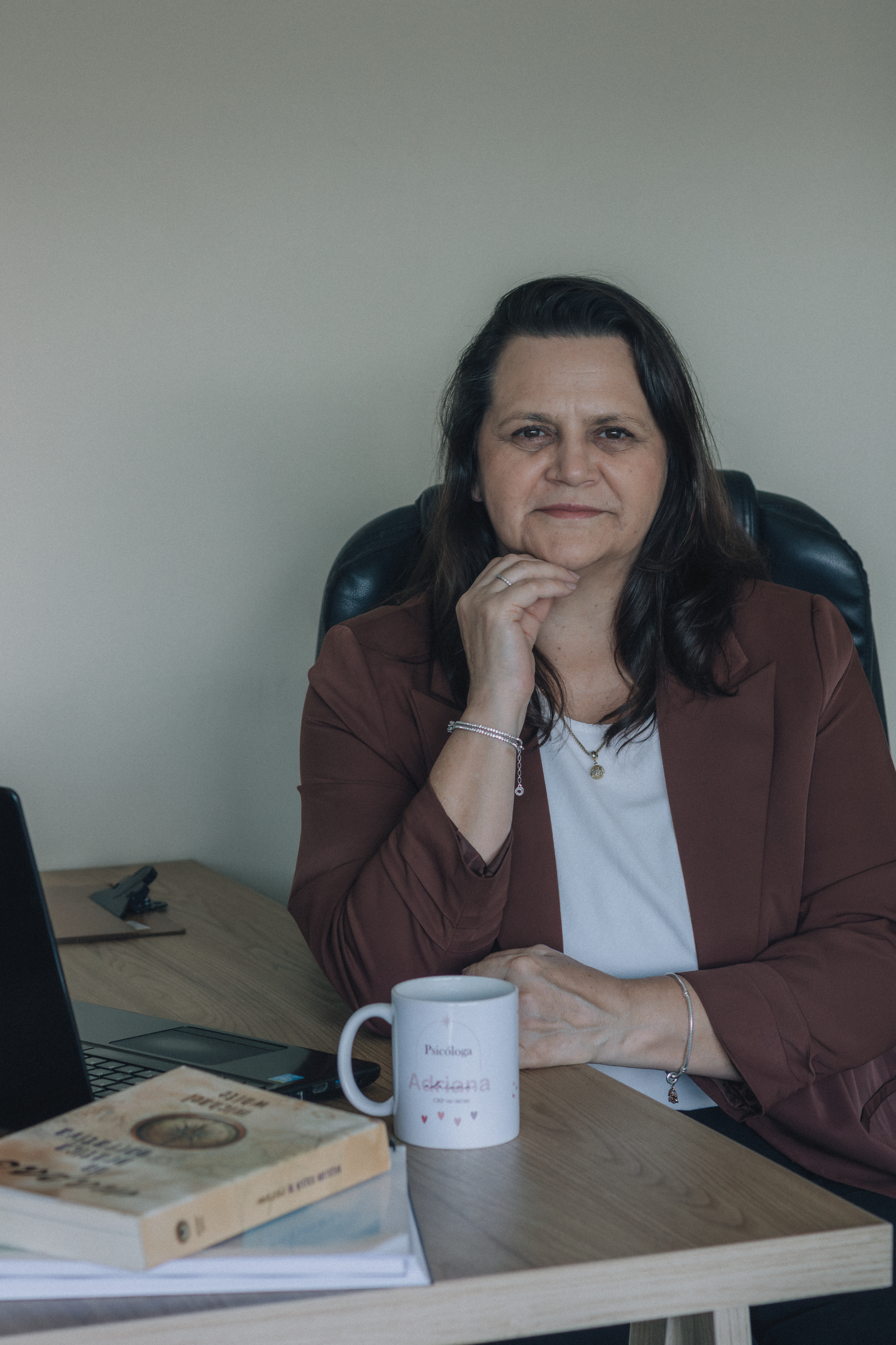 Confident adult woman sitting at a desk with laptop and coffee mug, conveying a professional atmosphere.