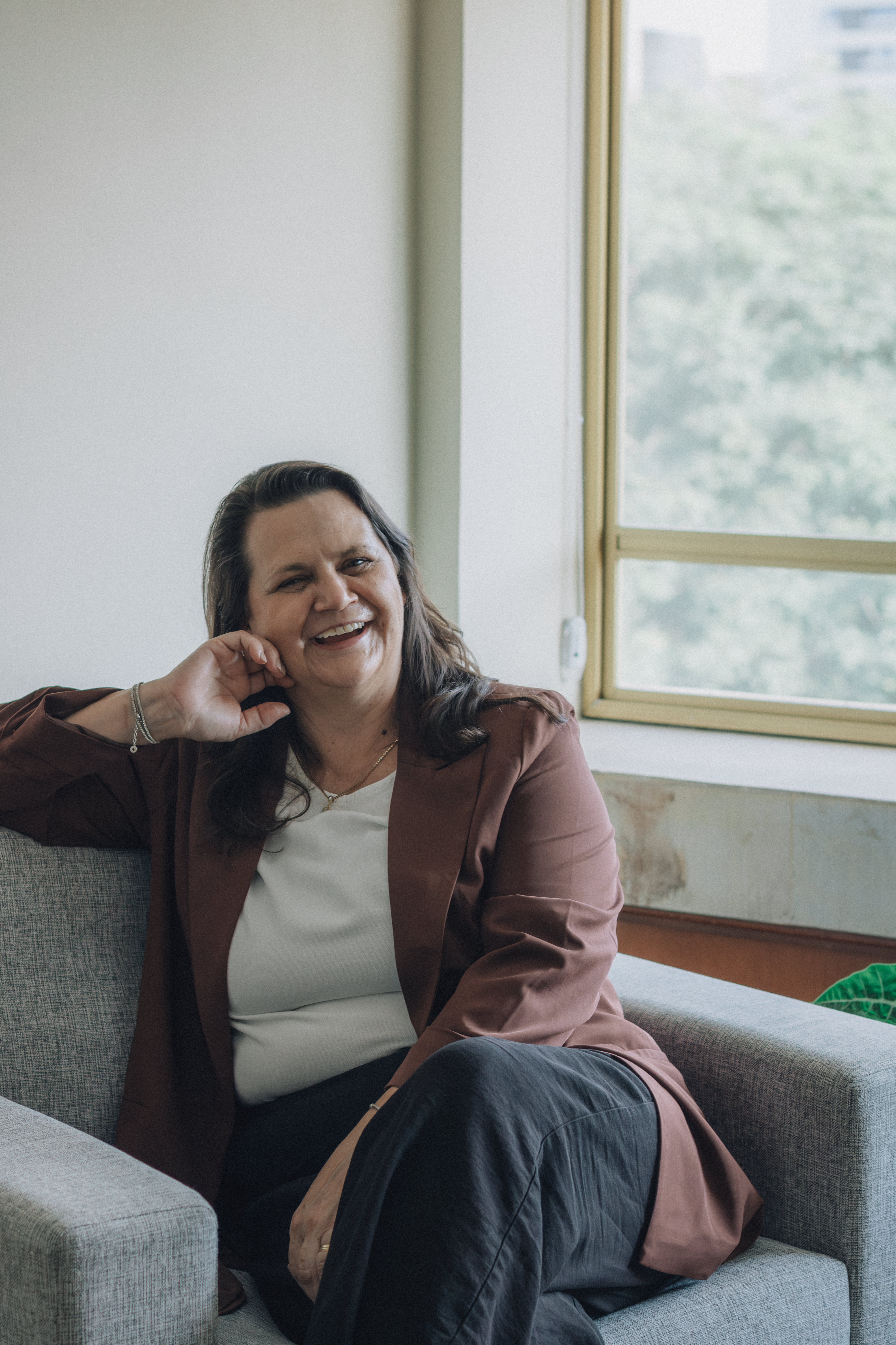 Woman smiling on a couch in a cozy indoor setting with natural light.