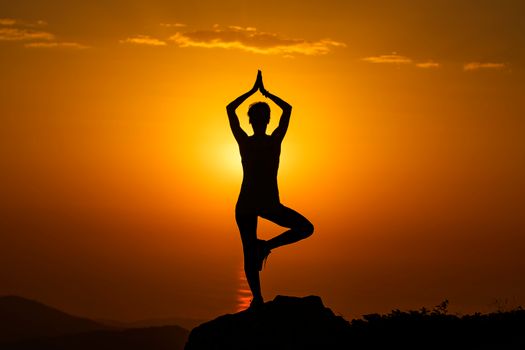 A serene silhouette of a person performing yoga at sunset on a mountain peak, symbolizing tranquility.