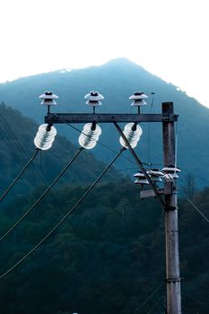 An electrical pole with insulators set against a misty mountain backdrop during daytime