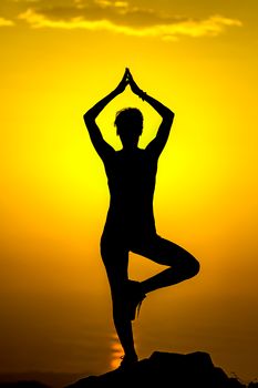 A serene silhouette of a woman in a yoga pose against a vibrant sunset sky.