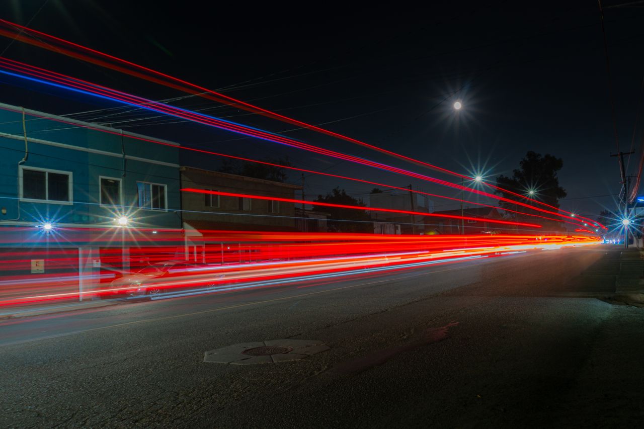 an urban street at night with dramatic red car light trails and a full