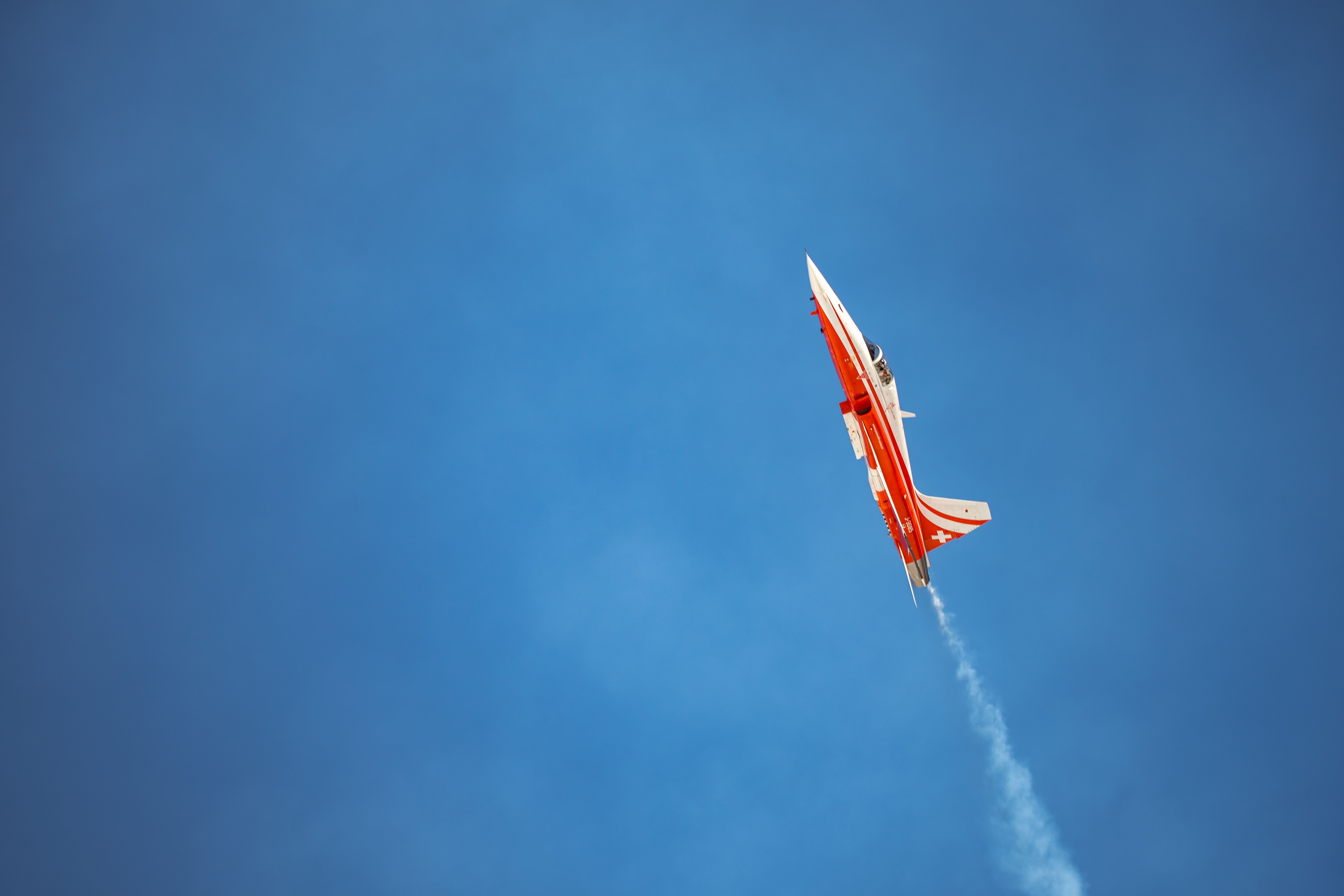 Red jet performing aerobatic flight against clear blue sky, showcasing precision and speed.