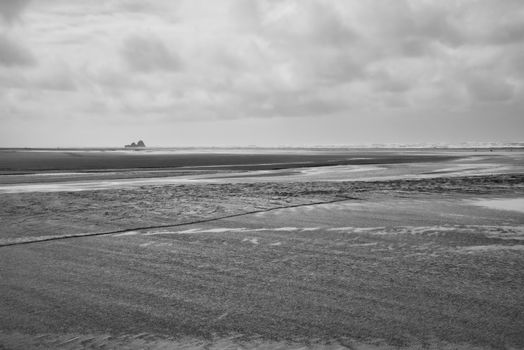 Black and white seascape with a moody sky and distant rock formations, creating a serene and dramatic scene.